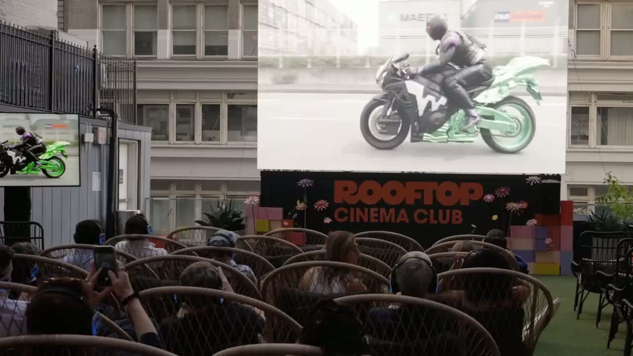 A rooftop cinema club screening at night, with a full audience watching a film outdoors